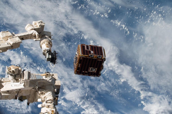 A robotic arm of the International Space Station extends toward a low-Earth-orbit satellite, with our planet seen in the background