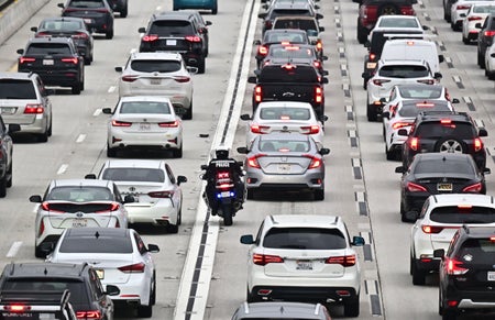 A motorcycle officer weaves through traffic through mostly black/white and silver cars.