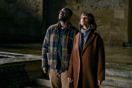 Male in plaid shirty and female in brown coat standing in empty space looking up.