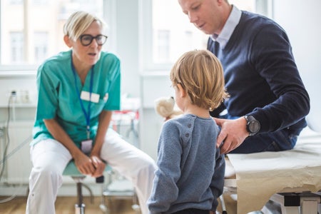 Rear view of boy standing by father while talking to doctor in clinic