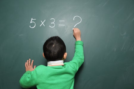 Young boy writes a math equation on a chalkboard, but unable to solve, "5x3=?"