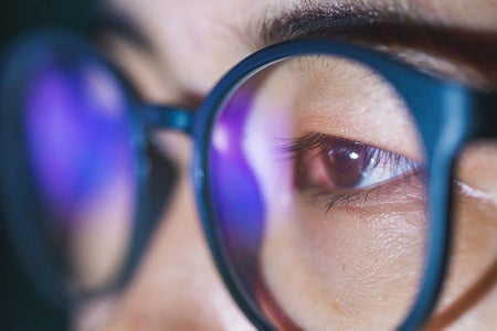 Close up of Young Asian man in glasses viewing computer dispay in the dark, blue light from display is reflected on the lenses