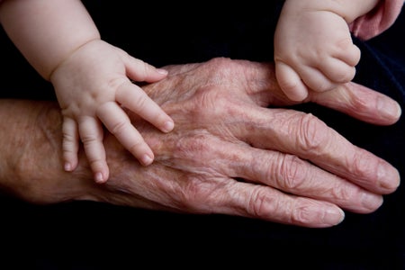 Elderly hand with baby hands shown on black backdrop.