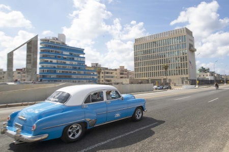 A robin-egg blue vintage car driving by buildings