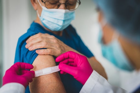 Nurse with pink gloves putting bandaid on a senior's arm.