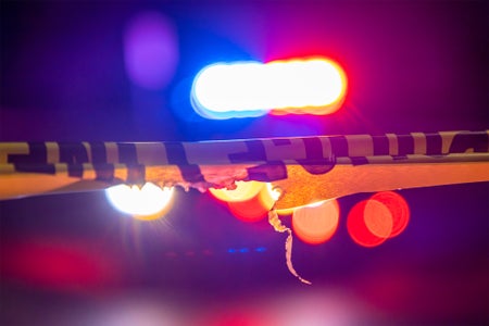 A defocused police car sits behind crime scene tape with flashing lights at night