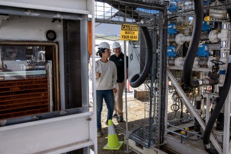 Female and male with with hard hat s looking at pipes inside a carbon capture pilot project.