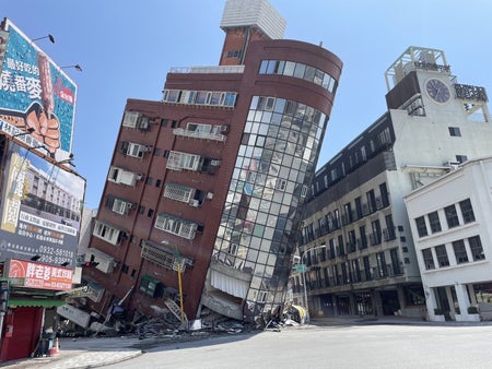 Tilted brown building with round section of windows at an intersection.